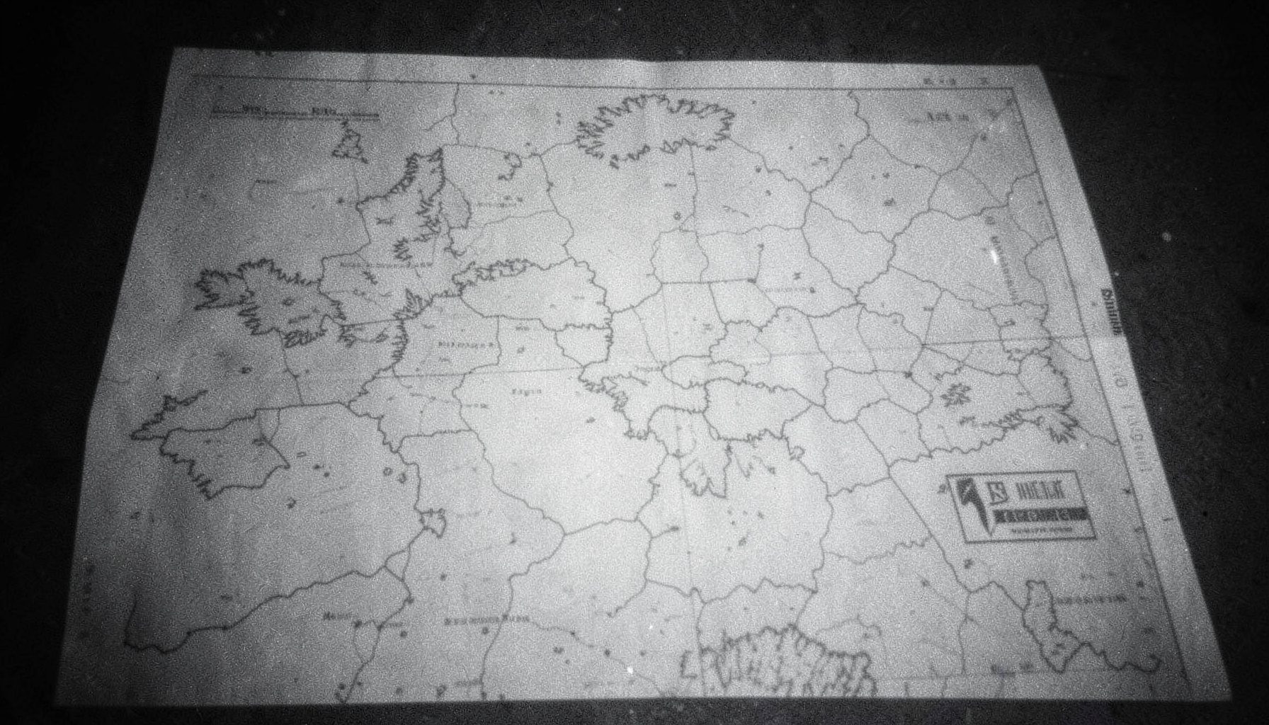 Fotografía analógica en tonos grises de un mapa impreso sobre una superficie oscura, con textura de grano fino y luz suave